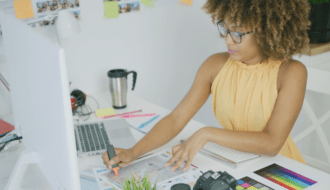 black woman with a yellow shirt at a desk for an article on self-confidence in entrepreneurship