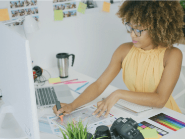 black woman with a yellow shirt at a desk for an article on self-confidence in entrepreneurship