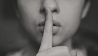 the bottom half of the face of a woman putting her pointer finger to her lips for an article encouraging readers to move in silence