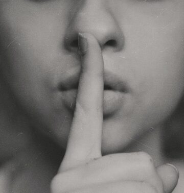 the bottom half of the face of a woman putting her pointer finger to her lips for an article encouraging readers to move in silence