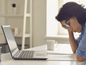 woman sitting at desk in front of a laptop with her hand to her head for article about how to overcome challenges