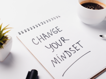 notebook opened to page with change your mindset written in it sitting on a desk with a small plant, a coffee mug and marker, for blog post about how to change your mindset