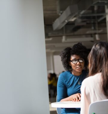 A black woman and a white woman sitting at a table across from each other for a blog article on how to assert yourself