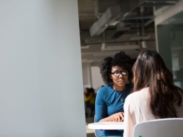 A black woman and a white woman sitting at a table across from each other for a blog article on how to assert yourself