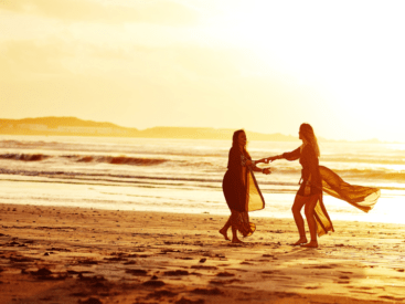 Two women dancing on the beach at sunset for a blog article about living life on your own terms.