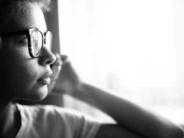 Black and white image of a woman wearing glasses with hand to her cheek gazing out of a window for a blog article about limiting beliefs
