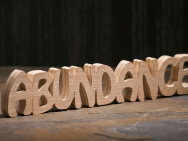 The word "abundance" is spelled out in wooden letters against a black background for a blog article about cultivating an abundance mindset.
